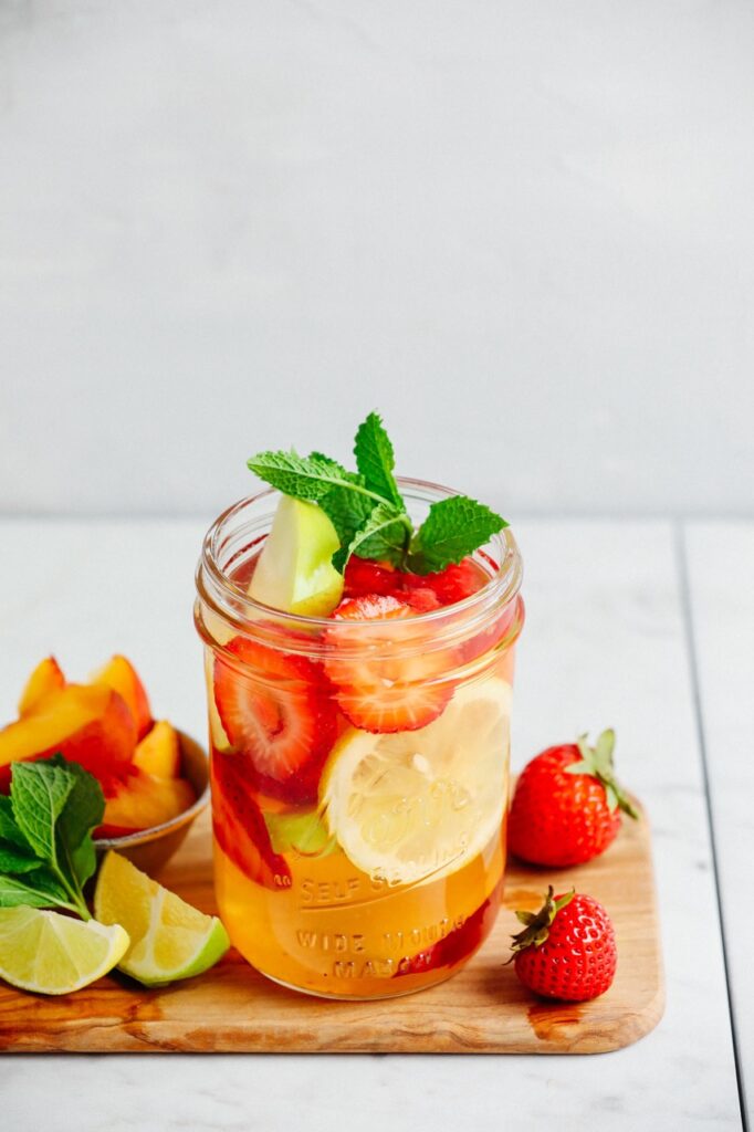 A traditional white sangria in a glass jar with lemons, strawberries, and limes.