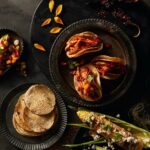 Zapotec Barbacoa de Pollo tacos on corn tortillas, served with spicy Elote street corn, pico de gallo, and dried chile peppers, showcasing the traditional Mexican autumn dish.