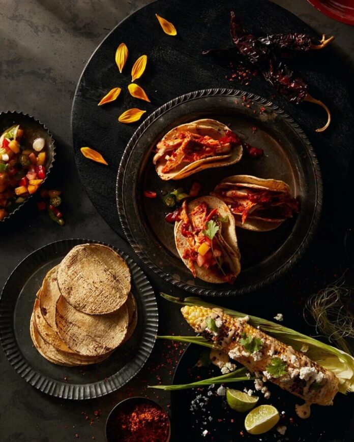 Zapotec Barbacoa de Pollo tacos on corn tortillas, served with spicy Elote street corn, pico de gallo, and dried chile peppers, showcasing the traditional Mexican autumn dish.