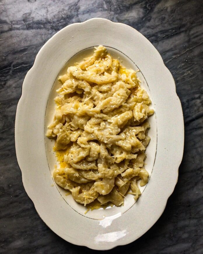 Gnocchi Sbatúi TABLE Magazine A white oval platter piled high with Gnocchi Sbatúi, or beaten gnocchi, covered in melted butter, cheese, and pepper, set on a dark, gray marble surface.