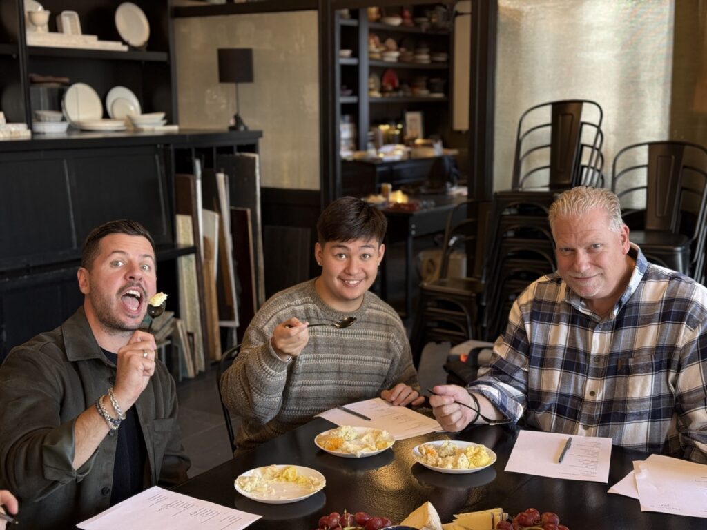 Three men sit at a table holding their forks up.