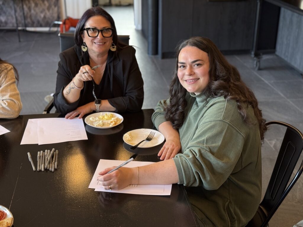 Two women sit at a table with plates of mashed potatoes.