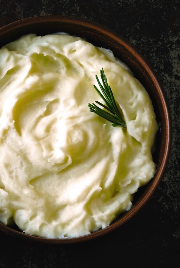 A bowl full of creamy mashed potatoes with a sprig of thyme in it.
