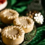 A close up shot of 3 pistachio tart desserts displayed on a glass cake plate with a green background.
