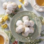 A green plate full of Pecan Balls stacked in a tower as some sit open with yellow cake on the table.