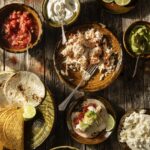 Various plates full of taco toppings like chicken, salsa, sour cream, lime juice, and more.