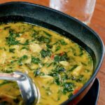A black bowl of Chicken and Orzo Soup with a silver ladle in it.