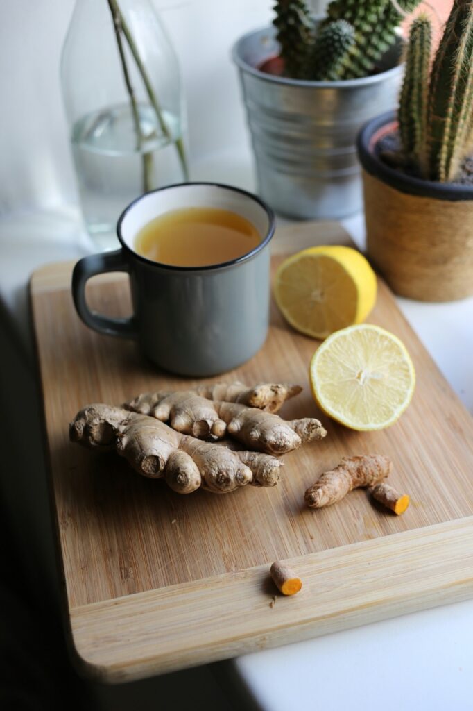 Ginger chopped up sits on a cutting board with sliced lemon and a cup of tea.
