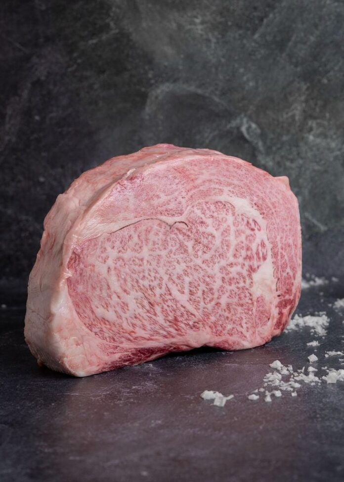 A chunk of marbled meat on a dark marble table with coarse salt all over the table.