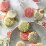 Cookies in green and pink sugars spread over a table and plate.