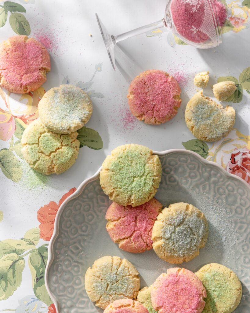 Cookies in green and pink sugars spread over a table and plate.