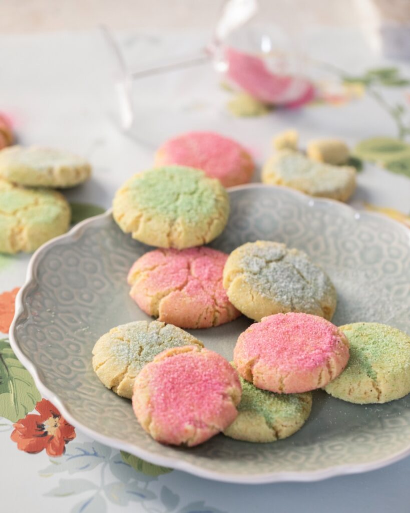A downward angle of pink and green sugar snickerdoodle cookies on a plate and around a table.