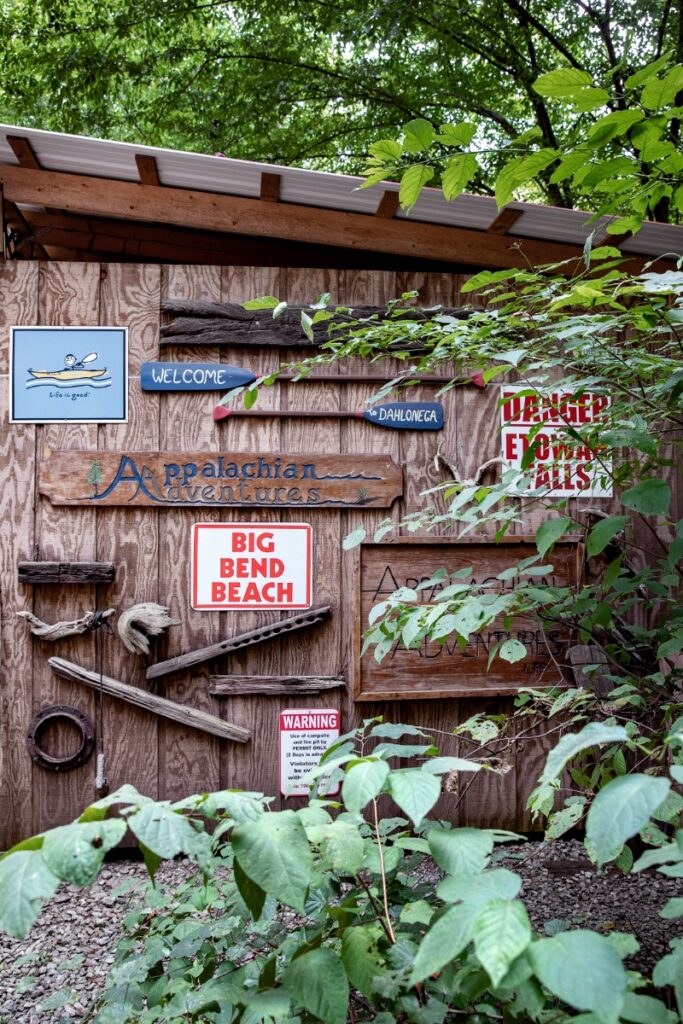 A rustic wooden wall decorated with adventure-themed signs including "Appalachian Adventures," "Big Bend Beach," and "Welcome to Dahlonega" at a Georgia river outfitter.