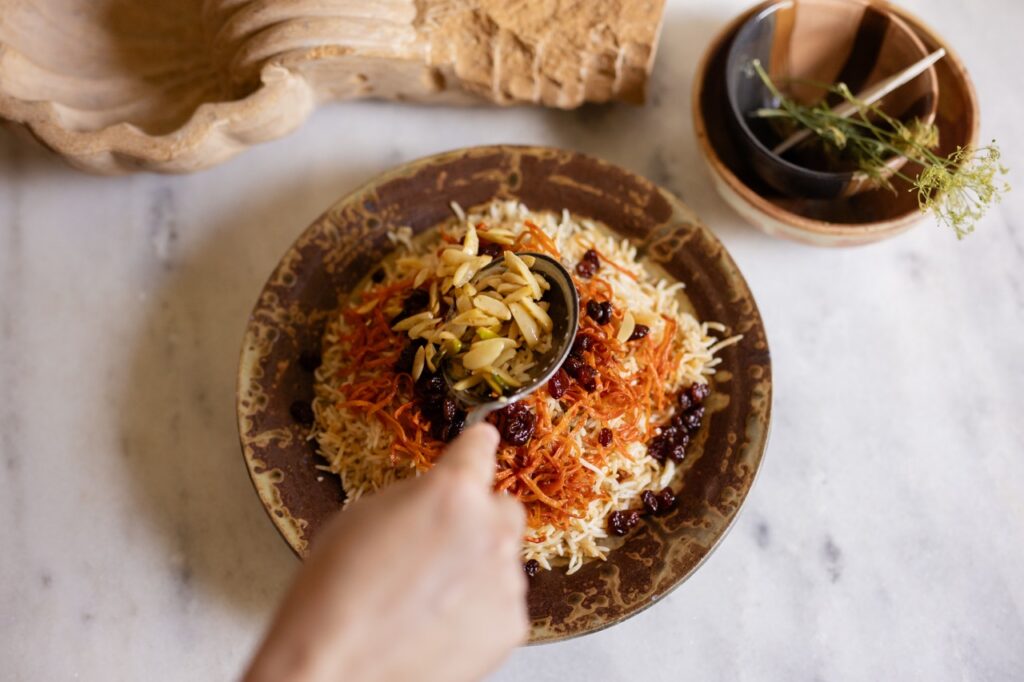 A person spoons a topping onto a bowl of Kabuli Pulao.