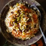 A black bowl full of Afghani Kabuli Pulao (Rice Pilaf) with nuts over top.