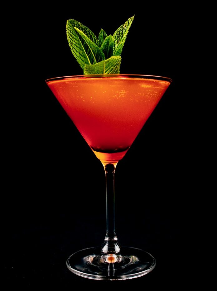 A martini glass with a red color cocktail and a mint garnish.