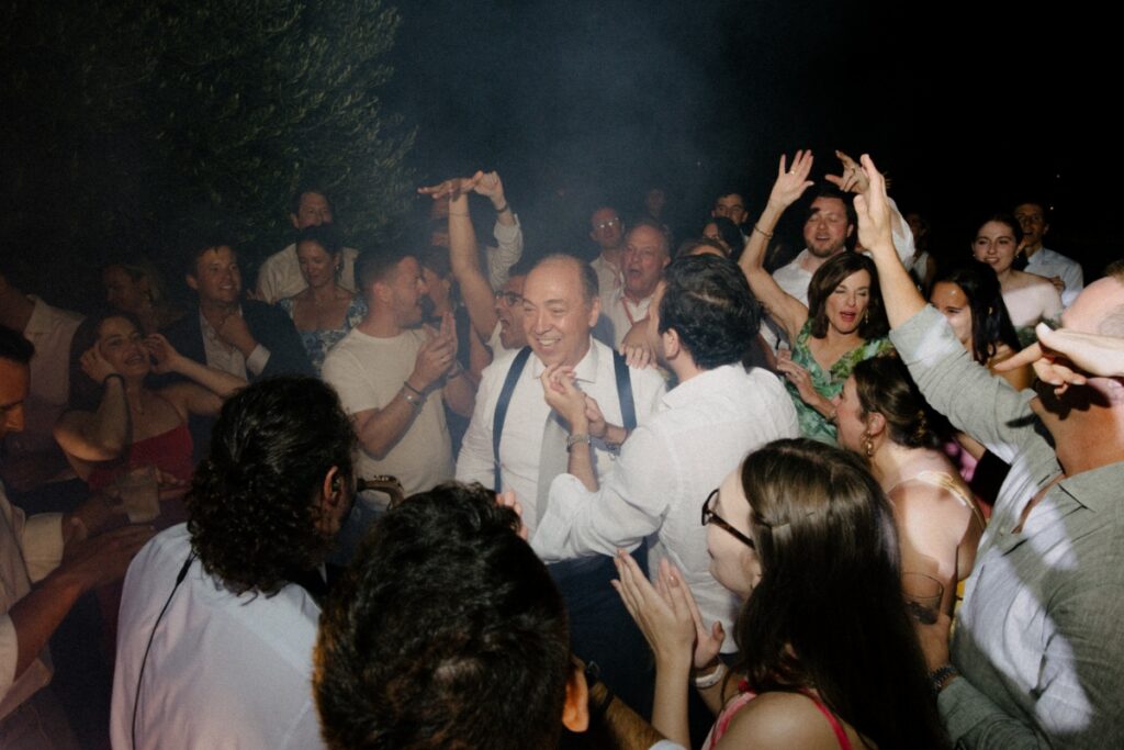 A candid photo of Joseph Bartolacci, the bride's father, dancing and laughing with guests during an energetic outdoor wedding reception at Relais Villa Corallo in Italy.