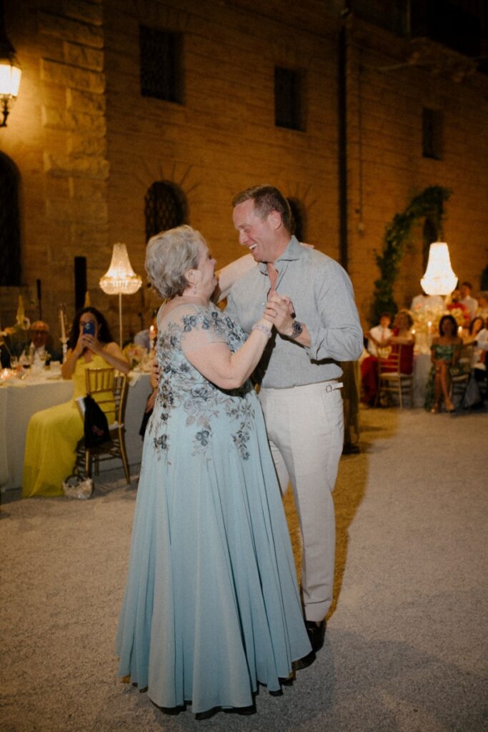 Groom Philip Caputo in a linen shirt and tan trousers dancing with a guest in a light blue floral gown.