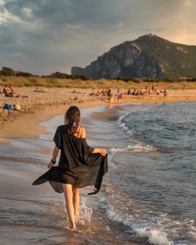 A girl in a dress walks down the coastline with water coming up over the sand.