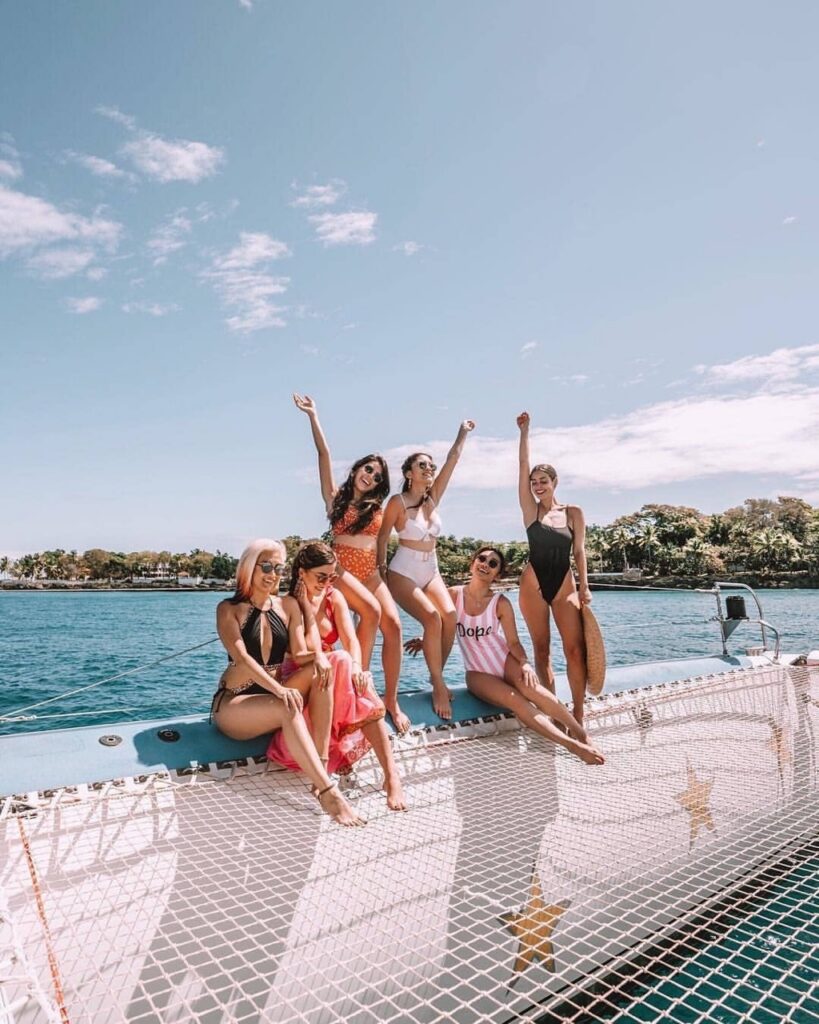 A group of girls sit on a netted boat on the blue water.
