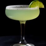 A green last word cocktail in a coupe glass with a lime wedge garnish.