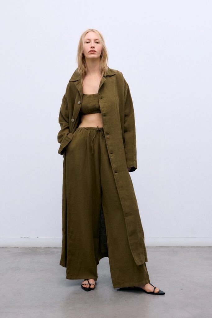 A woman in a long green trench coat with pants and top to match.