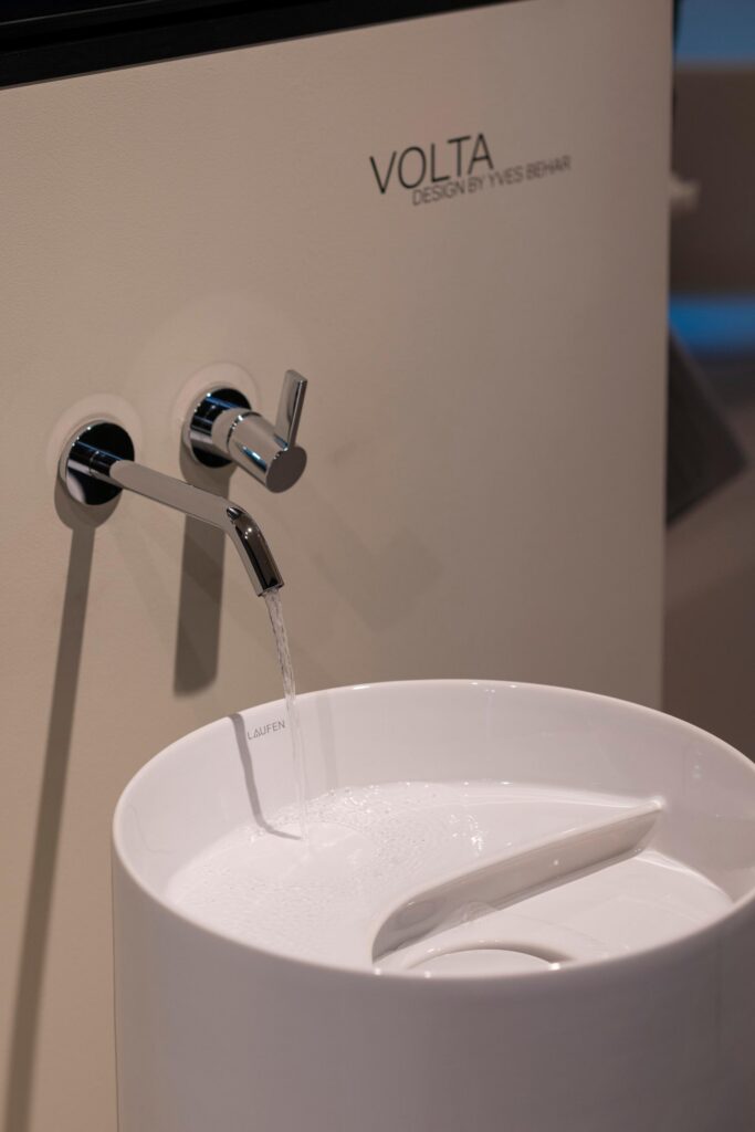 A white low sink below a silver faucet that water comes out of.