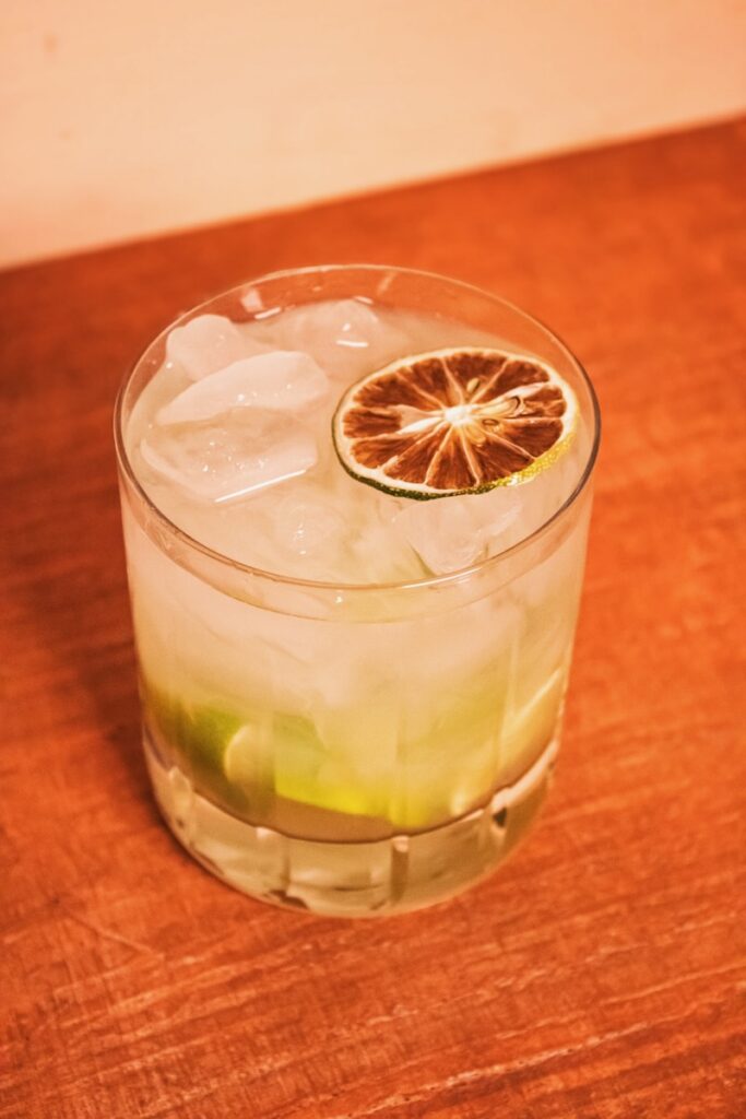 A short glass with lime wedges at the bottom, a lot of ice, and a dried lime wheel on top.