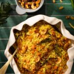 A white bowl full of a yellow rice pulav pilaf with carrots and curry leaves all through.