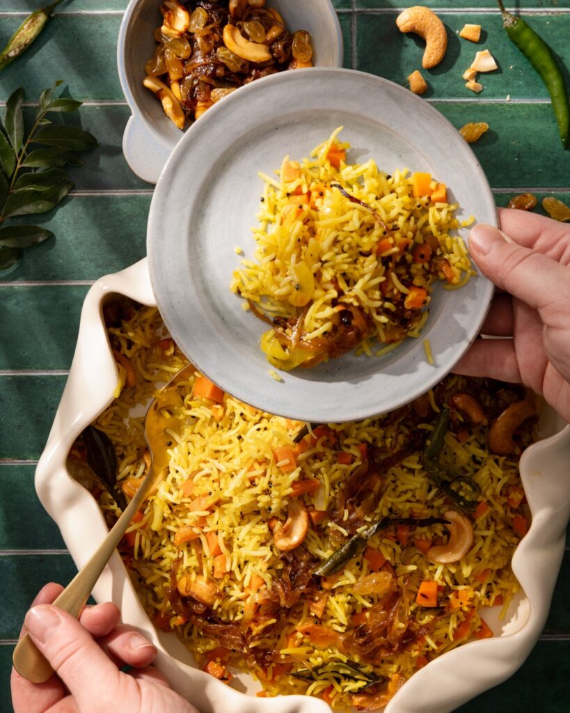 A person scoops spoonfuls of carrot pilaf onto a small plate.
