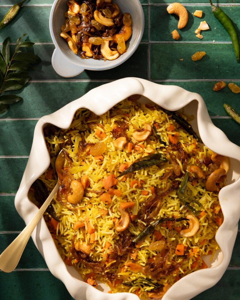 A white bowl full of a yellow rice pulav pilaf with carrots and curry leaves all through.