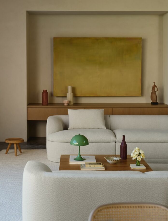 A beige couch sits in a living room with a table between it and another couch.
