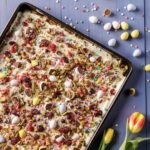 A tray of Easter Crack with half mini chocolate eggs everywhere, eggs above the tray and flowers below it.