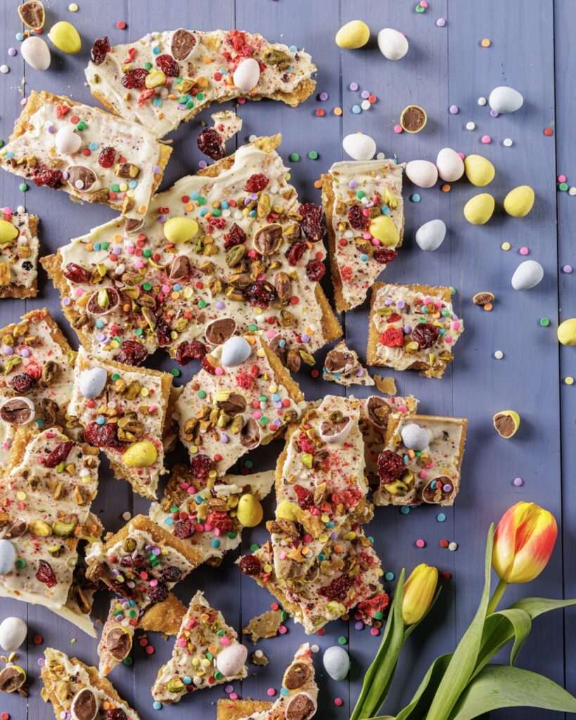 Easter Crack broken up on a purple table surrounded by flowers and mini chocolate eggs.