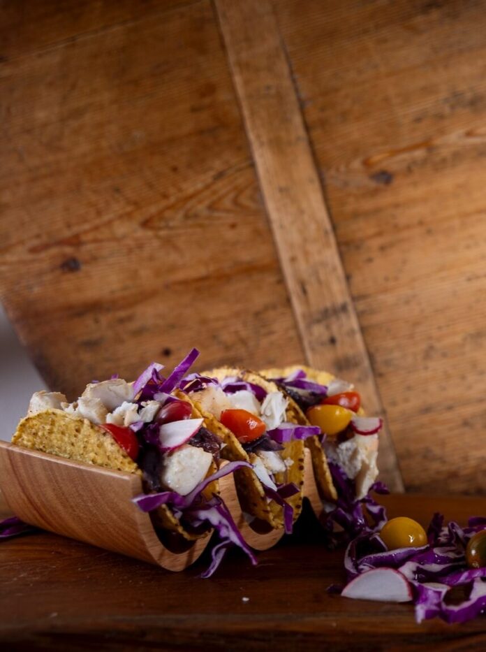 Three fish tacos in hard shells with purple slaw and tomatoes.