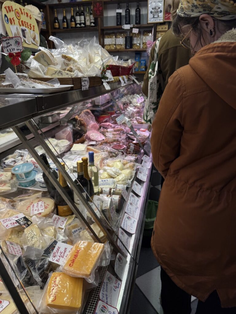 Cases of cheese as people walk by and look over them.