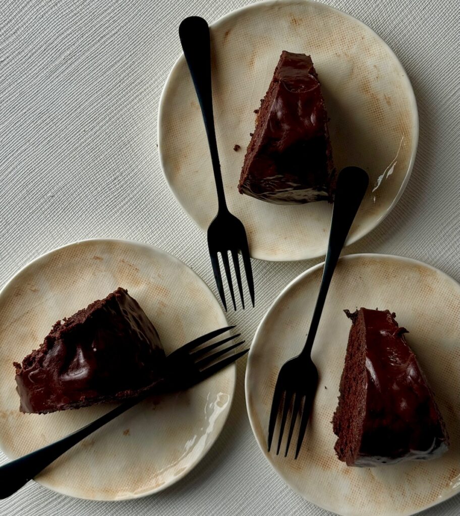 Three slices of dark chocolate cake sitting on three beige plates.