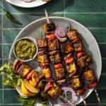 Skewers of Hariyali Paneer with vegetables on a plate with a green sauce beside it.