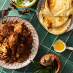 A place of roast chicken beside a cup of ghee and naan bread.