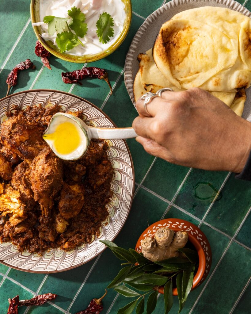 A person pours ghee over a Mangalorean Roast Chicken with naan above it.
