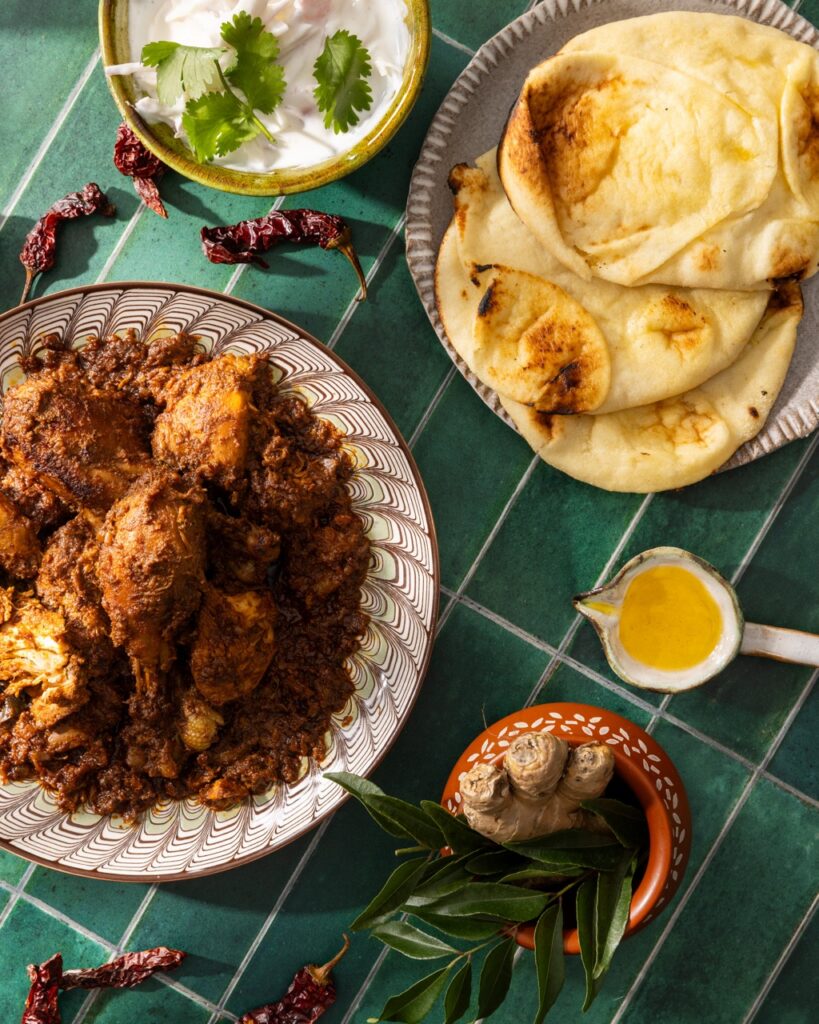 A place of roast chicken beside a cup of ghee and naan bread.
