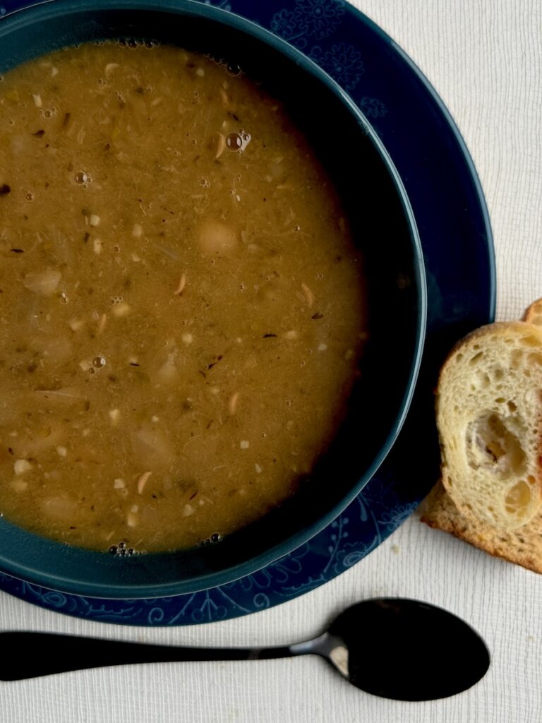 A bowl full of soup with a slice of bread on the side and spoon below it.