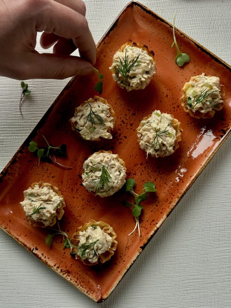 A rectangular orange tray with small chicken salad cups that a person is moving to grab.