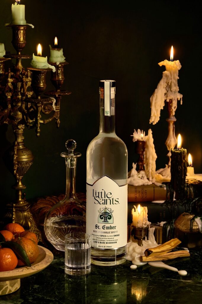 A bottle of Little Saints non-alcoholic gin sits on a table surrounded by candles.