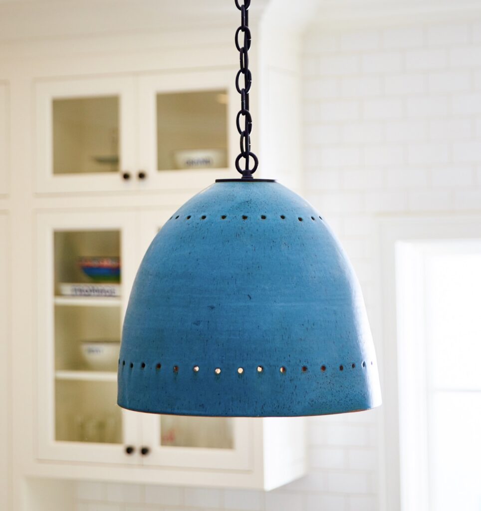 A hanging blue lamp beyond white cupboards.
