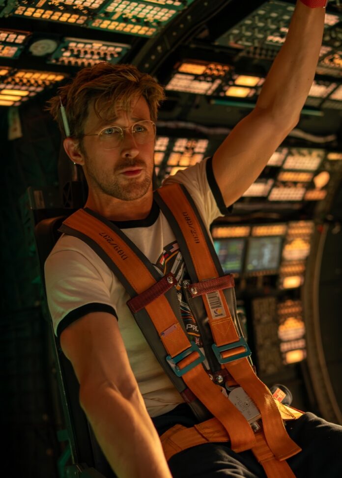 Ryan Gosling sits strapped into a spaceship with a pen behind his ear.