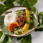 Plantains full of a meat filling beside a grapefruit slice and rice.