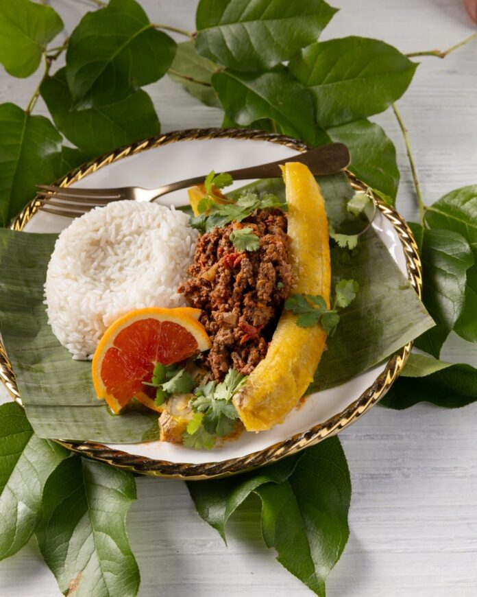 Plantains full of a meat filling beside a grapefruit slice and rice.