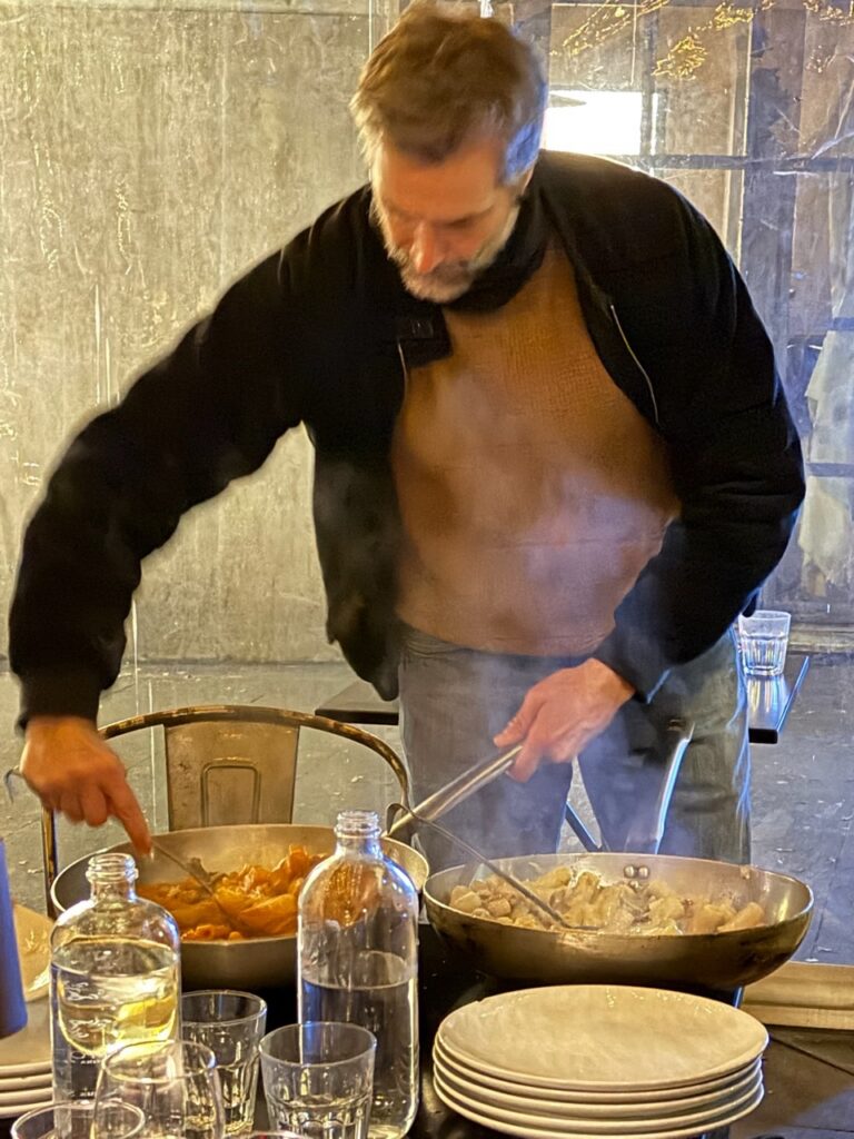 A man mixes up pasta at a table.