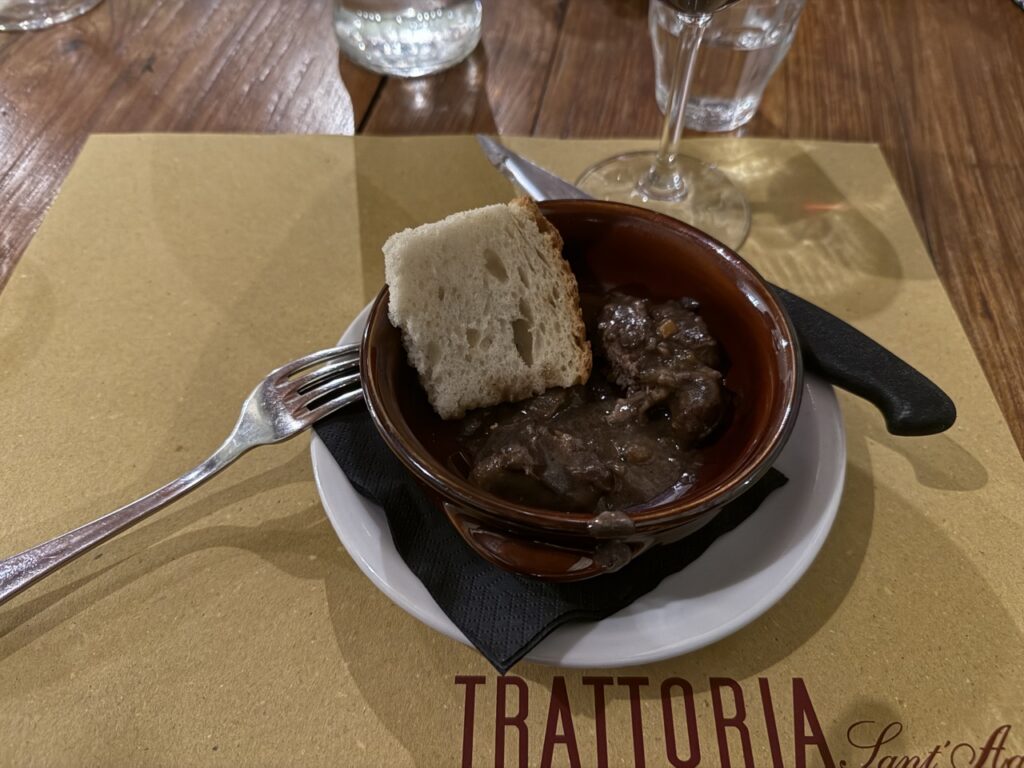 A bowl of beef stew with a chunk of bread and a fork sitting over it.